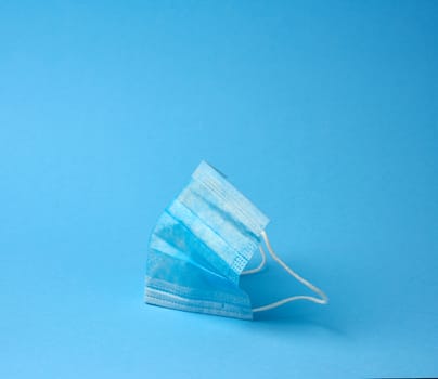 blue textile medical face mask with elastic bands folded, subject on blue background, element for designer