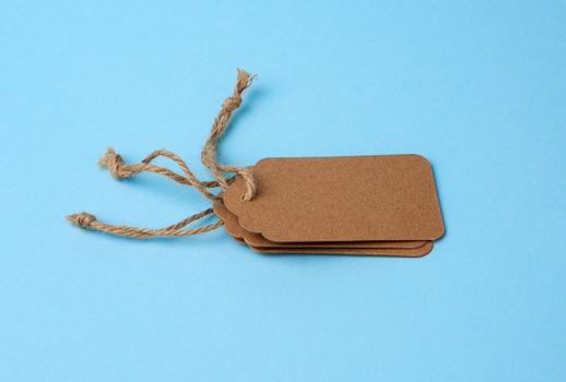 Empty brown paper tags tied with white string. Price tag, gift tag, sale tag  on the blue background, close up