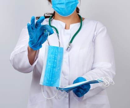 female doctor in a white coat and mask holds a stack of protective face masks about the virus, doctor stands on a white background