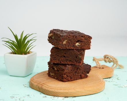 stack of square baked slices of brownie chocolate cake with walnuts on a wooden board, close up