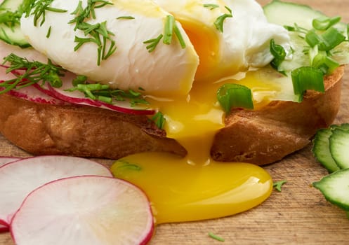 sandwich on toasted white slice of bread with poached eggs, dill and with slices of green onions, yellow yolk flows from the egg