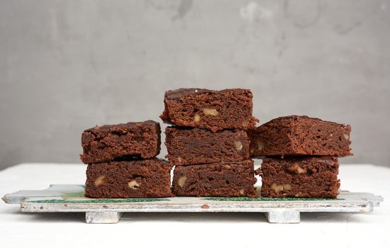 stack of square baked pieces of brownie chocolate cake with walnuts, on a wooden board