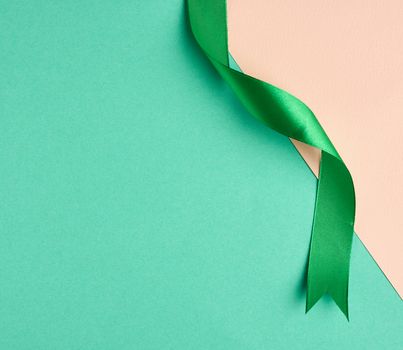 twisted silk green ribbon on a green-beige background, top view, cropped end