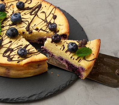 baked round cottage cheese casserole on a black plate, top view, tasty and healthy dessert
