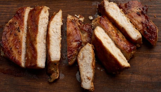 fried pork steak sliced on stripes on a kitchen cutting board, juicy well-fried meat, top view