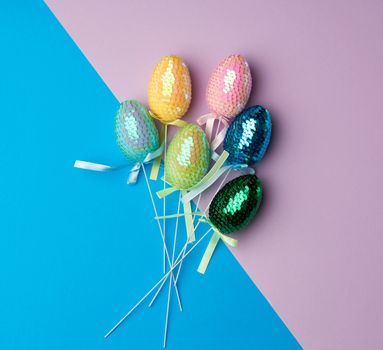 multicolored decorative Easter eggs decorated with sequins on a blue lilac background, festive backdrop, top view