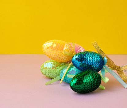multicolored decorative Easter eggs decorated with sequins on a color background, festive backdrop, top view
