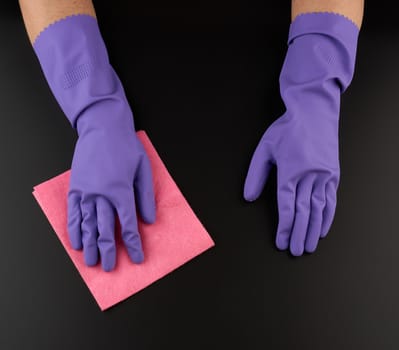 hand holds a pink rag sponge for cleaning, protective purple rubber glove is worn on the arm, black surface wash process