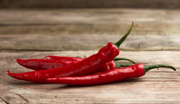 red chili peppers on a brown cutting wooden board, gray table, close up