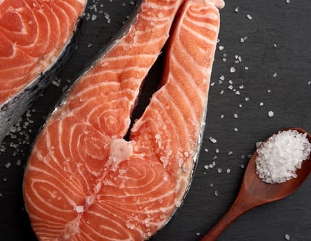 raw salmon steaks with white salt on a black background, top view