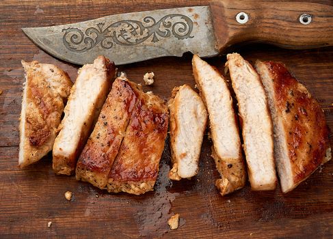 fried pork steak sliced on stripes on a kitchen cutting board, juicy well-fried meat, top view
