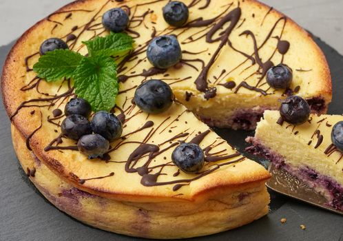 baked round cottage cheese casserole on a black plate, top view, tasty and healthy dessert