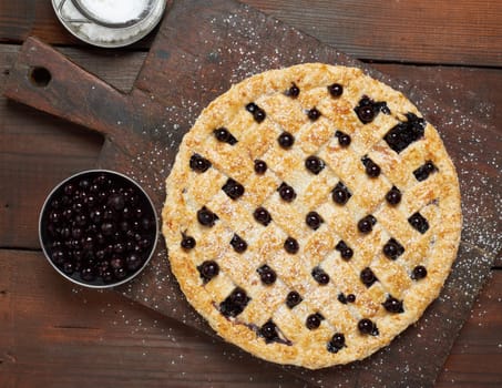 baked round black currant pie on wooden background, top view
