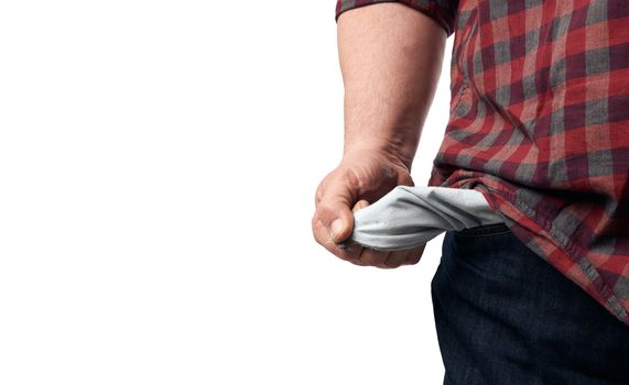 man in a red plaid shirt turned out the empty pockets of his pants, concept of poverty and crisis, unemployment, copy space