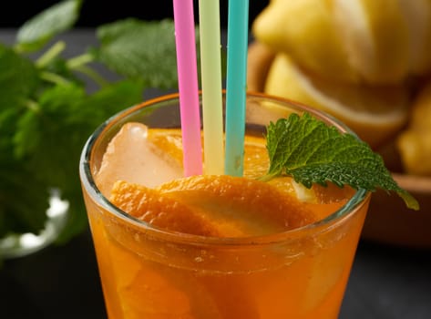 glass with a handle filled with lemonade with slices of orange and lemon, behind a bunch of green mint, black background