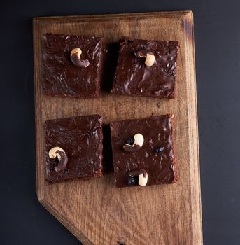 square baked slices of brownie chocolate cake with walnuts on a brown wooden surface. Cooked homemade food. Chocolate pastry. Sweet meal, homemade dessert