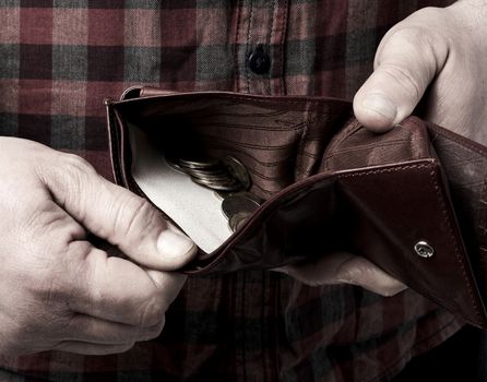 man holds an open brown leather wallet with Ukrainian hryvnia coins, poverty concept, close up