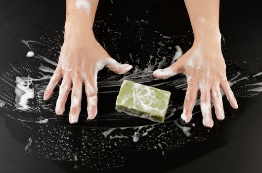 process of washing hands with blue soap, parts of the body in white foam on a black background, top view, hygiene concept