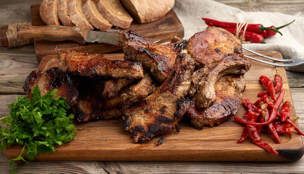 grilled pork steaks on the bone on a kitchen cutting board, baked sliced rye flour bread,  top view