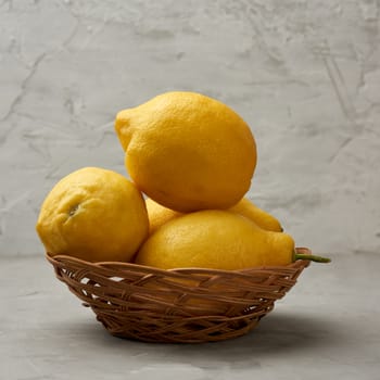 ripe yellow lemons in a wicker basket on a gray table, ingredient for lemonade