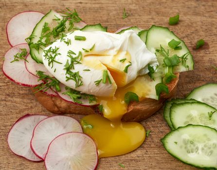 sandwich on toasted white slice of bread with poached eggs, green leaves of onion, morning breakfast on a brown wooden board, close up