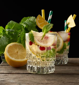 transparent glass with lemonade and pieces of ice, red berries, a refreshing summer drink on a black background 