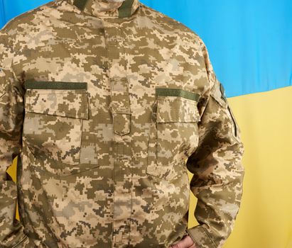 Ukrainian man a warrior dressed in a military pixel uniform stands against the background of the national flag of Ukraine