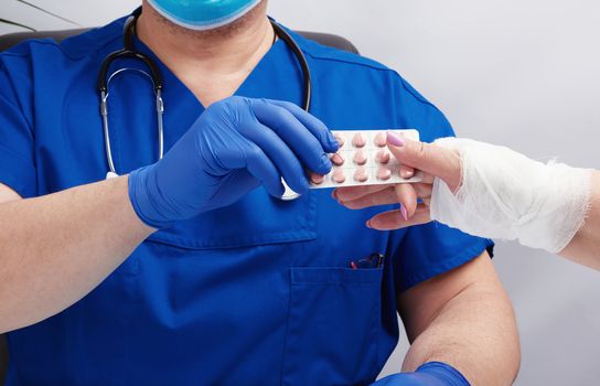 doctor in uniform and blue latex medical gloves sits at a table and examines a patient with a hand injury, doctor gives painkillers, office for patients