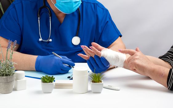traumatologist doctor in blue latex medical gloves sits at a table and holds a patient reception with a hand injury, doctor's workplace