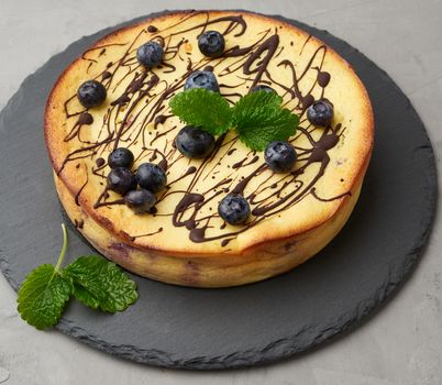 baked round cottage cheese casserole on a black plate, top view, tasty and healthy dessert