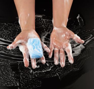 process of washing hands with blue soap, parts of the body in white foam on a black background, top view, hygiene concept