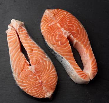 two raw salmon steaks on a black background, top view