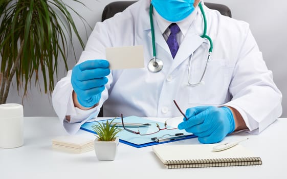doctor in a white medical coat sits at a table in a brown leather chair and holds a rectangular white blank business card in his hands, medical office