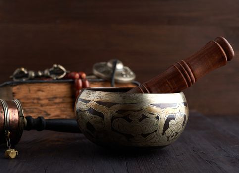 Tibetan singing copper bowl with a wooden clapper on a brown wooden table, objects for meditation and alternative medicine, close up
