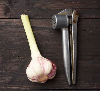 old metal garlic press and fresh young white garlic on a brown wooden table, top view