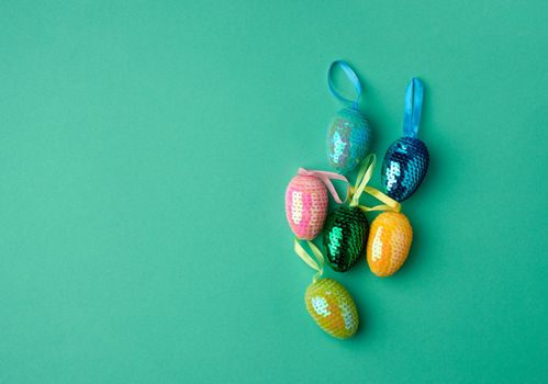 multicolored decorative Easter eggs decorated with sequins on a green background, festive green background, top view, copy space