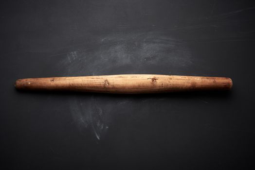 very old wooden rolling pin for rolling dough on a black background, top view