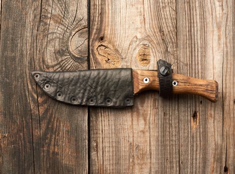 vintage kitchen knife with a wooden handle lies in a leather case on a wooden table from old boards, top view