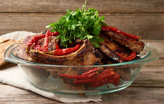 grilled pork steaks on the bone lie in a transparent glass plate on a wooden table, barbecue