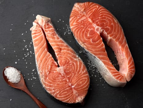 two raw salmon steaks with white salt on a black background, top view