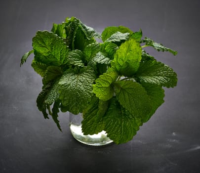 bunch of fresh green mint stands in a glass bowl on a black table, fragrant seasoning for food and cocktails