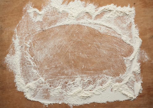 white wheat flour scattered on a brown wooden table, top view, kitchen backdrop, copy space