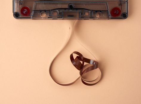 cassette with a brown magnetic tape on a beige background, the tape is tangled, top view