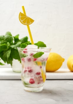 transparent glass with lemonade and pieces of ice, red berries on a white background, a refreshing summer drink
