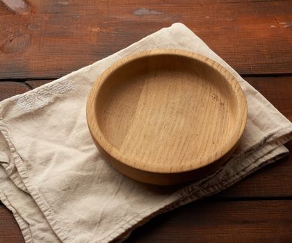 empty round brown plate standing on a gray linen napkin, wooden background from old boards, top view