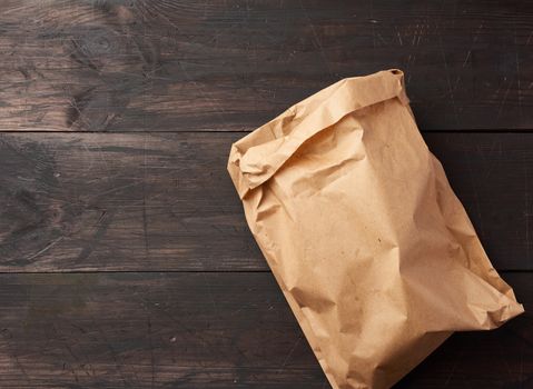 open brown paper bag for food packaging on a brown wooden background, concept of rejection of plastic bags to save the environment, top view