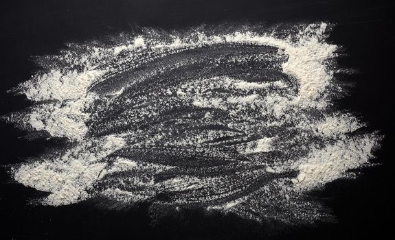 white wheat flour scattered on a black wooden table, top view, kitchen backdrop, copy space