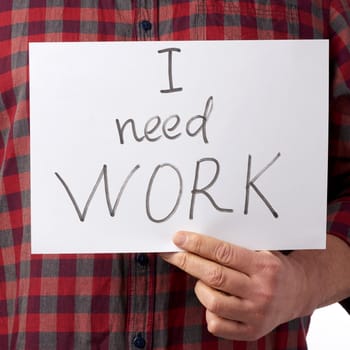 man in a red shirt and jeans holds a piece of paper with the inscription i need work, concept of unemployment against the backdrop of the global crisis, fired employee, man is isolated on a white