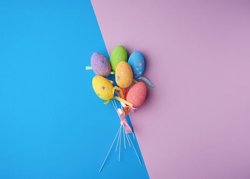 multi-colored decorative Easter eggs on sticks on a blue lilac background, festive backdrop, top view, copy space