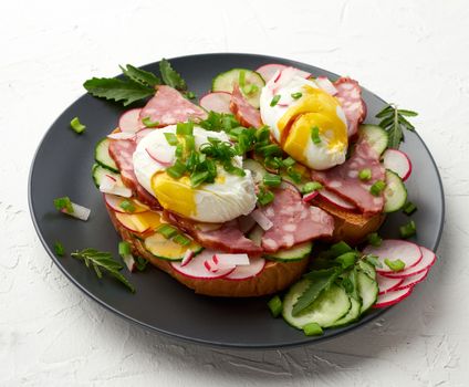 sandwich on toasted white slice of bread with poached eggs, green leaves of arugula, cucumber and radish, morning breakfast on a round plate, white background, eggs benedict 